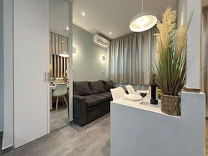 Een moderne woonkamer met een grijze bank, een eettafel met stoelen, een grote potplant en een hanglamp.