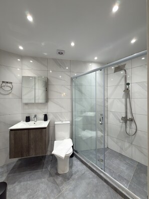 A modern bathroom with a glass shower enclosure, a marble-tiled wall, a wooden cabinet, and a toilet. - SmartLiving Central Apt 3 (Thessaloniki)