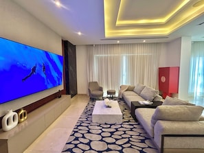 Ein modernes Wohnzimmer mit Flachbildfernseher, einer Couch, einem Couchtisch und einem gemusterten Teppich.