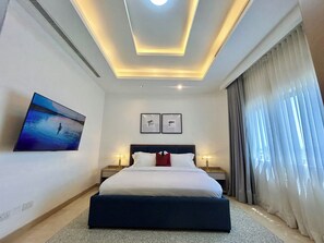 Una habitación de hotel moderna con una cama grande, una lámpara de techo, una mesita de noche, una lámpara y un cuadro en la pared.