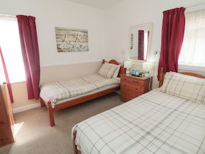A bedroom with two beds, a dresser, a nightstand, a mirror, and a wall-mounted picture. - Meltham Guest House (Scarborough)