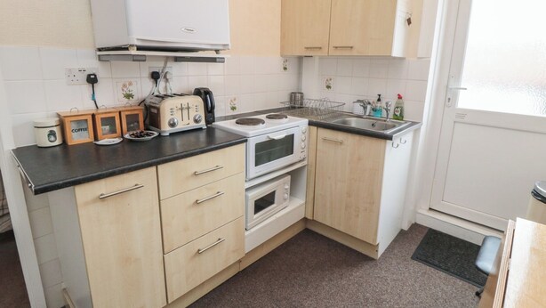 A compact kitchen with a stove, oven, and toaster. There is a sink and a window. - Meltham Guest House (Scarborough)