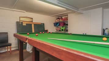 A pool table with balls, a chair, and a shelf with toys.