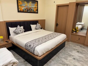 A neatly made bed with a patterned bedspread, a headboard, and a nightstand with a lamp. - Hotel Shri Radhavan (Mathura)