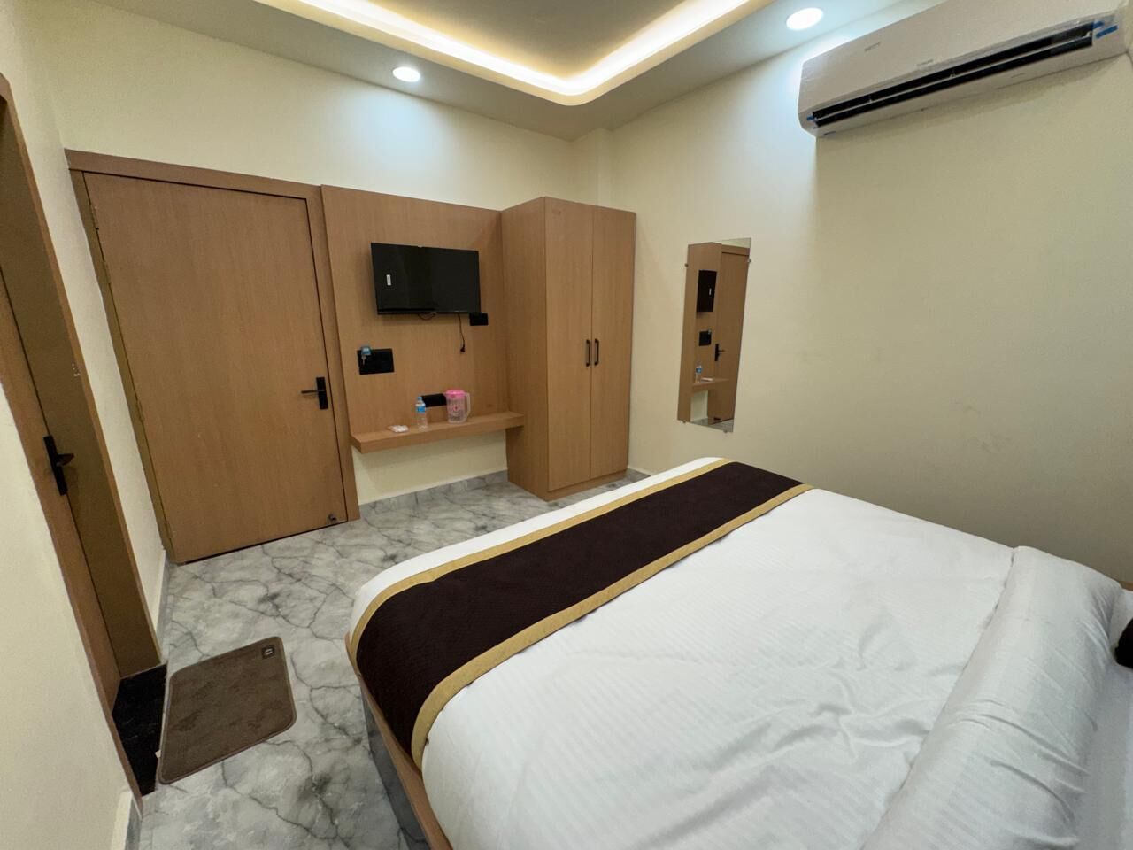 Una habitación de hotel con cama, armario de madera, televisor montado y aire acondicionado.