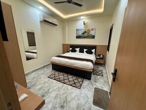 A bedroom with a bed, bedside tables, an air conditioning unit, a ceiling fan, a painting, and a marble floor. - Hotel Shri Radhavan (Mathura)