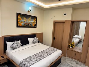 A hotel room with a bed, a nightstand, a wall-mounted artwork, a wardrobe, and a mirror. - Hotel Shri Radhavan (Mathura)