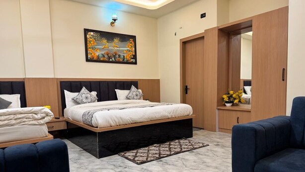 A modern bedroom with a bed, two nightstands, a dresser, a mirror, and a seating area. - Hotel Shri Radhavan (Mathura)