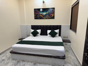 A bedroom with a bed, headboard, nightstands, a wall-mounted painting, and marble flooring. - Hotel Shri Radhavan (Mathura)