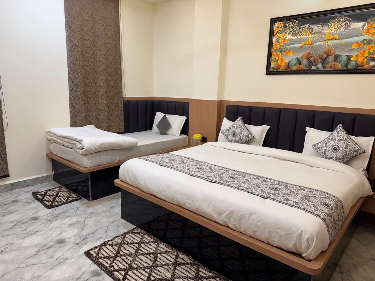 Una habitación de hotel con una cama grande, una cama más pequeña, un cabecero, una obra de arte colgada en la pared y una alfombra estampada.