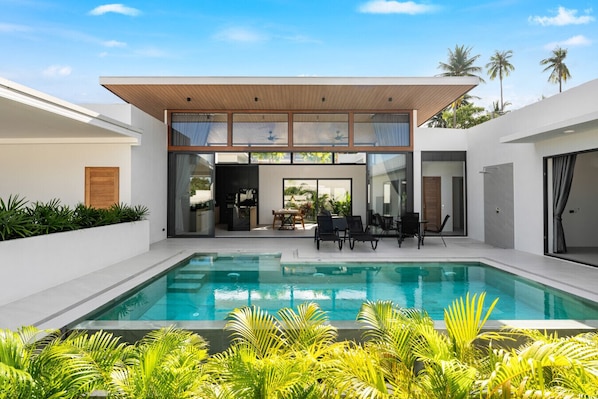 Ein modernes Haus mit Swimmingpool, Sitzgelegenheiten im Freien und einer überdachten Terrasse.
