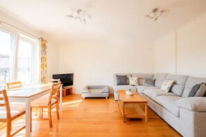 Un salon comprenant un canapé, une table à manger avec des chaises, un téléviseur et un ventilateur de plafond.