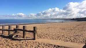 En sandstrand med et træhegn, en klar himmel og fjerne bakker.