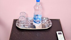 Una bandeja con una botella de agua, un vaso y una calculadora sobre una superficie de madera oscura contra un fondo rosa.