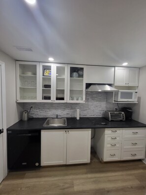 Cozinha compacta com armários brancos, micro-ondas, torradeira, pia e lava-louças.