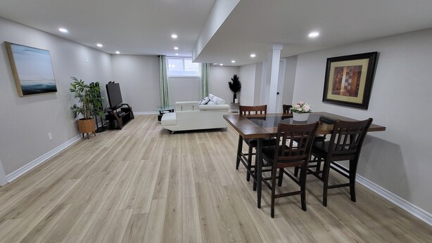 A spacious living area with a dining table, chairs, a sofa, a TV, and a potted plant. - Cozy 2-bedroom Basement Unit Near Calypso Water Park Embrun (Embrun)