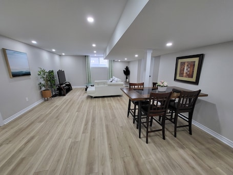 A spacious living area with a dining table, chairs, a sofa, a TV, and a potted plant.. Cozy 2-bedroom Basement Unit Near Calypso Water Park Embrun
