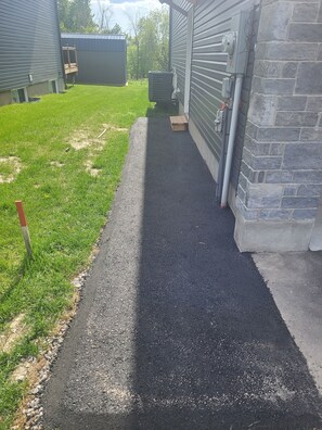 A paved pathway leading to a building with a stone wall and an air conditioning unit.