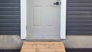 A white door with a keypad lock, set in a gray exterior wall with horizontal siding. - Cozy 2-bedroom Basement Unit Near Calypso Water Park Embrun (Embrun)