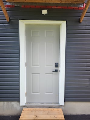 A white door with a keypad lock, set in a gray exterior wall with horizontal siding.