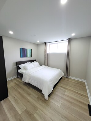 Um quarto com cama, janela com cortinas, um quadro na parede e uma luminária no teto.