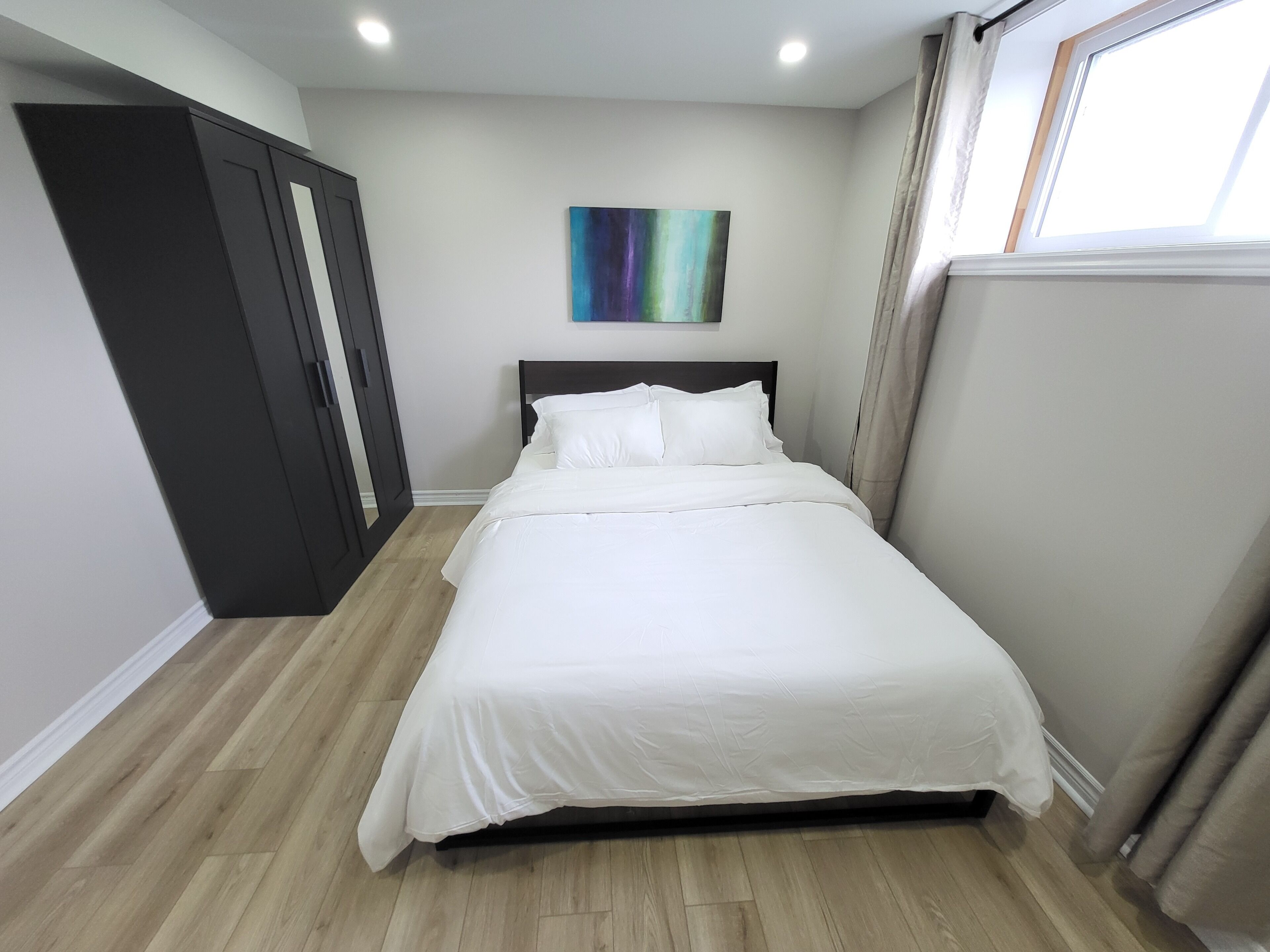 Un dormitorio con cama, armario, un cuadro y ventana.
