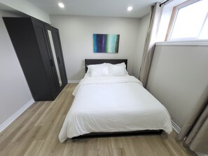 A bedroom with a bed, a wardrobe, a painting, and a window. - Cozy 2-bedroom Basement Unit Near Calypso Water Park Embrun (Embrun)