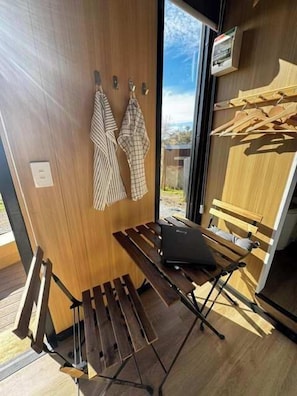 A wooden bench with a laptop, a wooden wall with a window, and a drying rack with clothes. - The Dairy and Pines Tiny house by Tiny Away (Guyong)