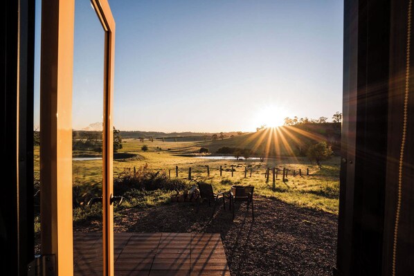 A view through a window of a rural landscape with a fence, a bench, and a small body of water.