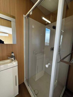 A shower with a glass door, a sink with a mirror, and wooden paneling. - The Dairy and Pines Tiny house by Tiny Away (Guyong)