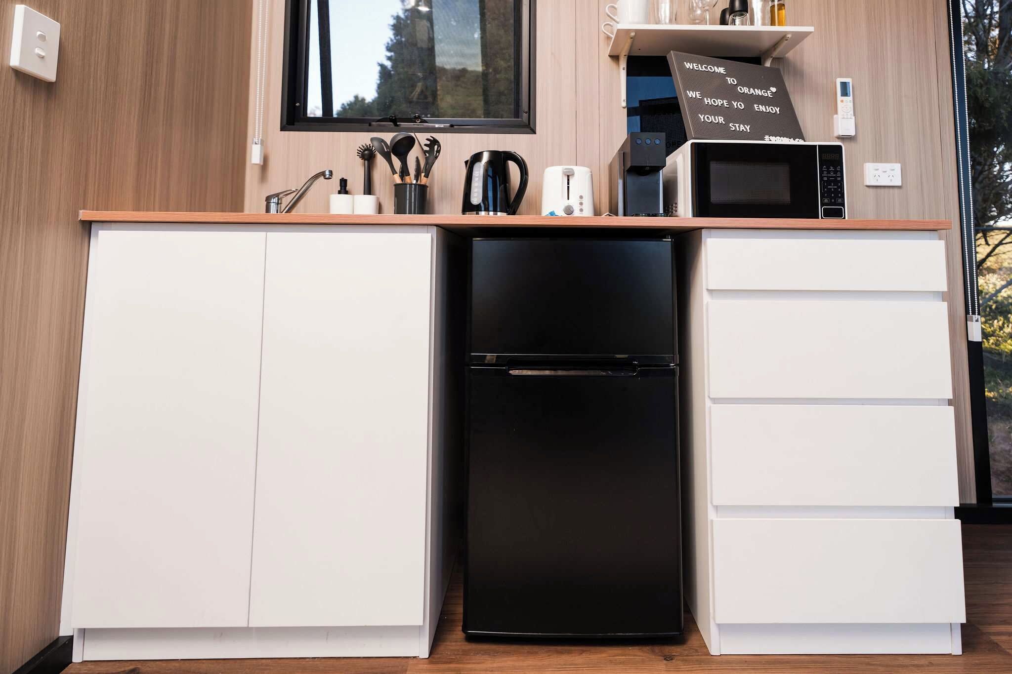 A compact kitchen with a black refrigerator, white cabinets, and a window above the sink.