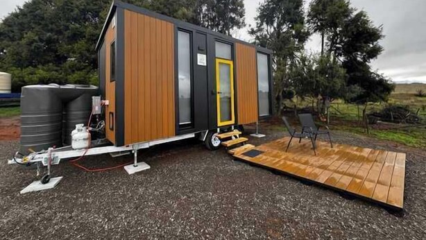 Ein modernes, kompaktes Wohnmobil mit Holzfassade, einer Schiebetür und einer kleinen Terrassenfläche.