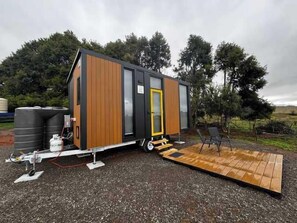A modern, compact mobile home with a wooden exterior, a sliding door, and a small deck area.