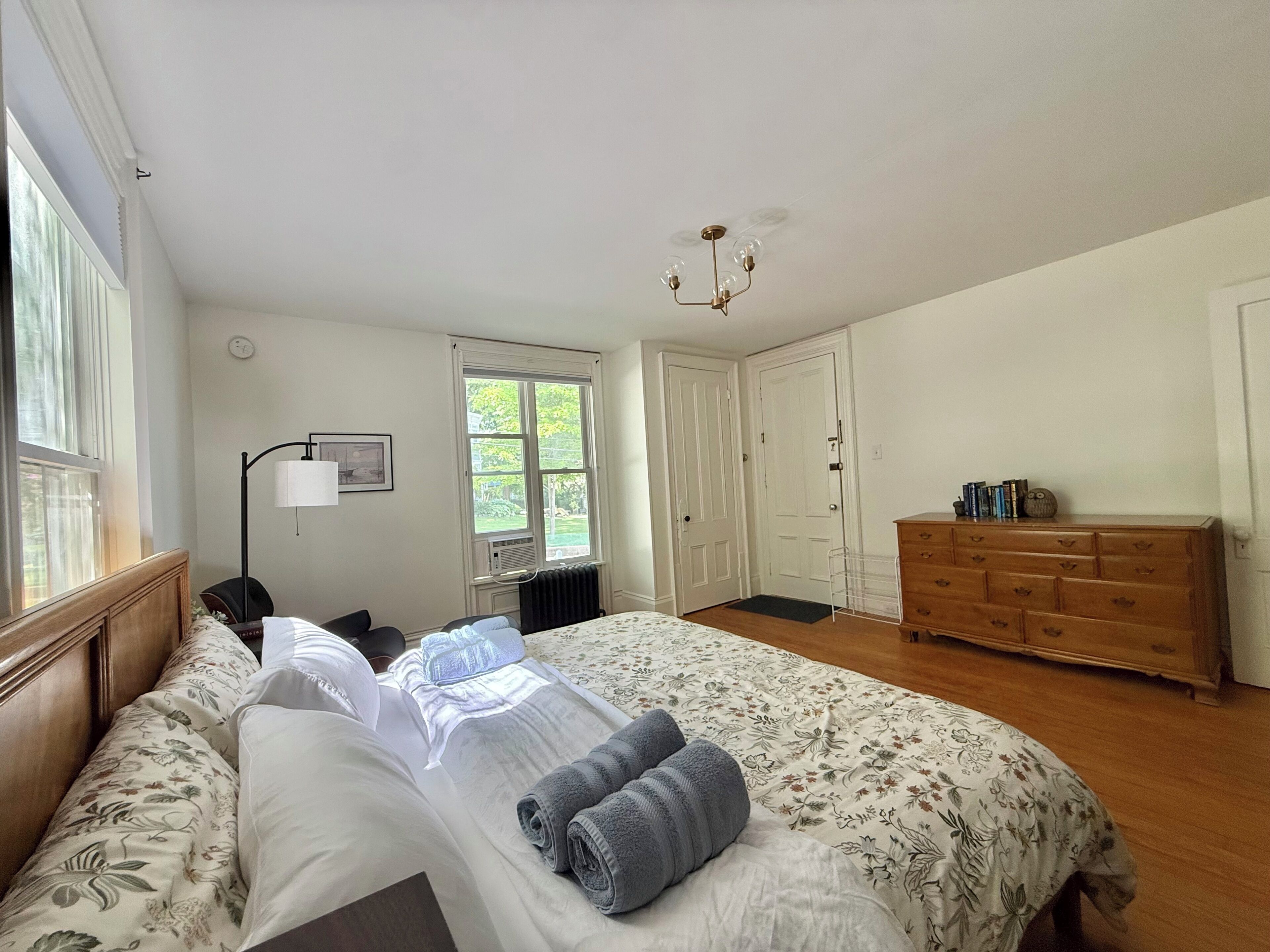 A bedroom with a bed, bedside table, lamp, dresser, and a window.