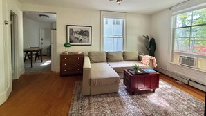 Una sala de estar con un sofá modular, una mesa de centro, un aparador, un cuadro en la pared y una ventana con persianas.