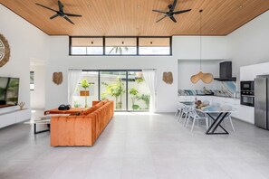 A modern interior with a sofa, dining table, kitchen, and large windows. - Villa Mona | Stylish 3BR Pool Villa (Bo Put)