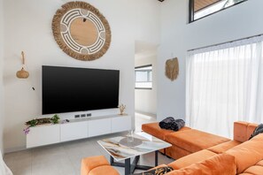 A modern living room with a large flat-screen TV, a round wall decoration, and orange furniture. - Villa Mona | Stylish 3BR Pool Villa (Bo Put)