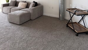 A modern living room with a sectional sofa, a small wooden side table with glasses, and a large mirror on the wall.