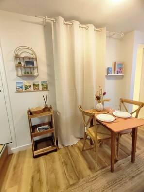 Un comedor con una mesa de madera, sillas, un estante pequeño con libros y una cortina.