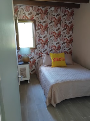 Een slaapkamer met een bed, nachtkastje, lamp en raam.