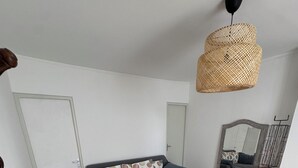 Ett vardagsrum med en soffa, ett soffbord, en fåtölj i rotting, en hängande lampa och en öppen spis.