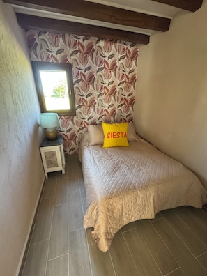 Een slaapkamer met een bed, nachtkastje, lamp, raam en een wand met bloemenprint.
