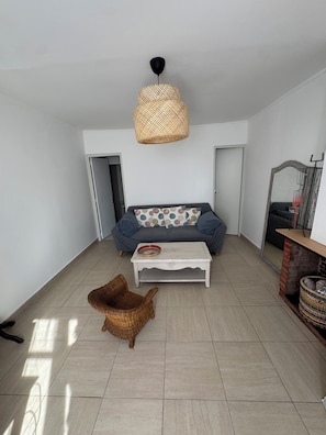 A spacious living room with a sofa, a coffee table, a wicker chair, a hanging light fixture, and a fireplace. - Vrbo Property (Valençay)