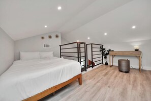 Ein Schlafzimmer mit einem Bett, einem Schreibtisch, einem Mülleimer und einer Pflanze.
