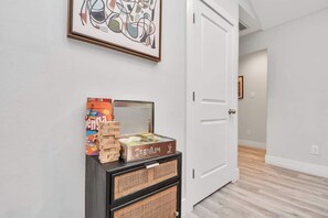 A hallway with a white door, a framed abstract painting, a box of Jenga, and a Cranium game box on a black wicker console. - 3BR w loft | Near I MDanderson l TMC, UH & NRG (Houston)
