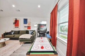 Ein Wohnzimmer mit einem Shuffleboard-Tisch, einer Couch, einem Couchtisch und einem Basketballkorb.