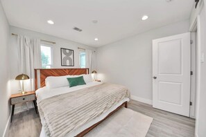 A bedroom with a wooden headboard, a bed with white bedding, a green pillow, two bedside lamps, a white door, and a window with curtains. - 3BR w loft | Near I MDanderson l TMC, UH & NRG (Houston)