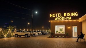 Ein Hotel namens 'Hotel Rising Ayodha' mit einer Reihe geparkter Autos davor.