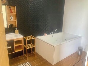 A modern bathroom with a large bathtub, wooden shelves, a sink, and a textured wall. - Vrbo Property (Puerto Carrillo)