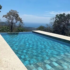 A rectangular infinity pool with a clear blue tile pattern, surrounded by a light-colored deck. - Vrbo Property (Puerto Carrillo)
